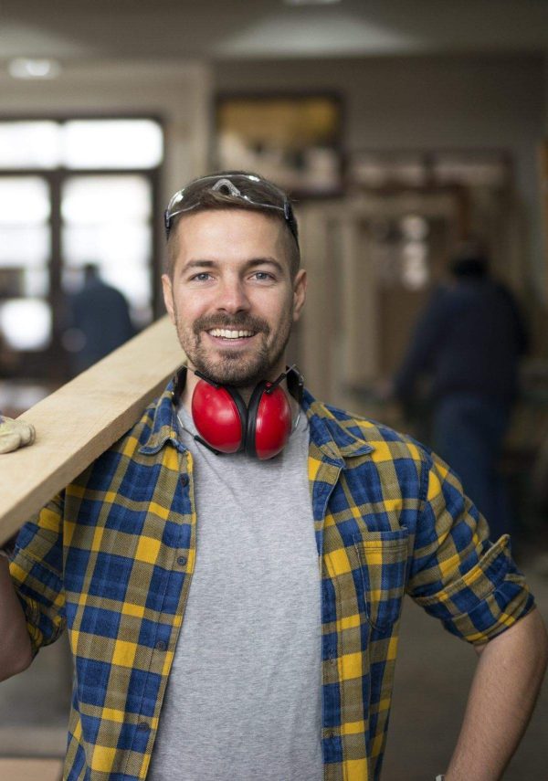 Portrait of handsome smiling carpenter with wood material at workshop.